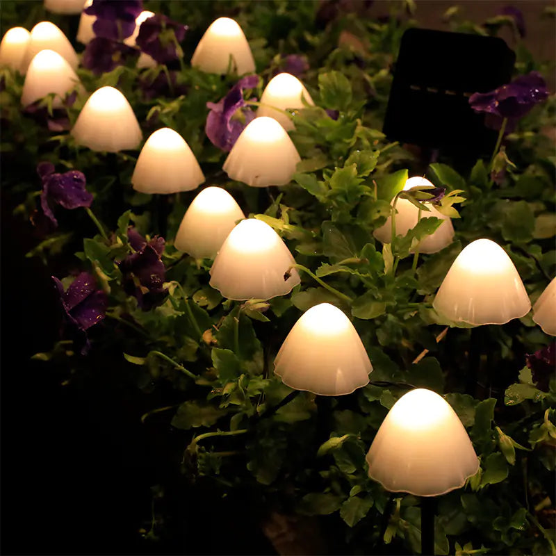 Mushroom-shaped solar lights on a bed of green plants and purple flowers