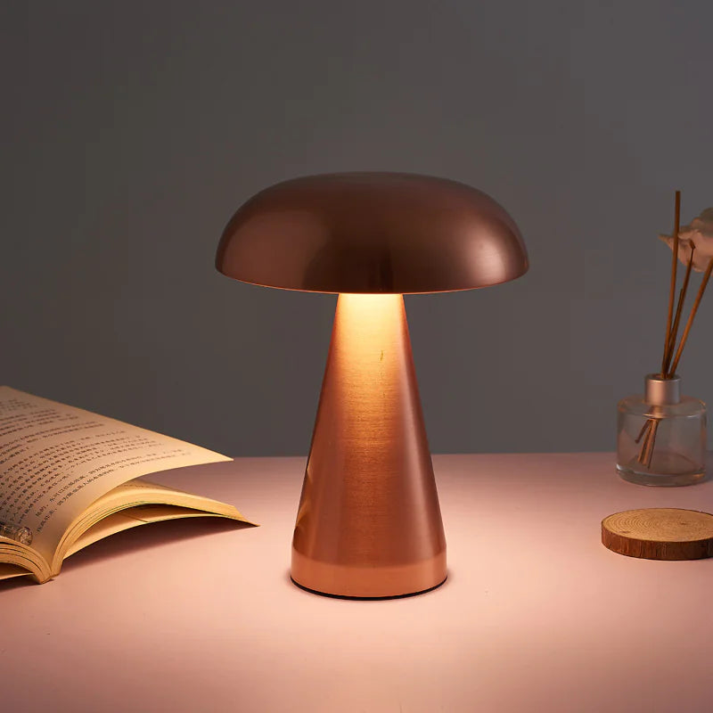 Mushroom-shaped table lamp on a table with an open book and a vase in the background.