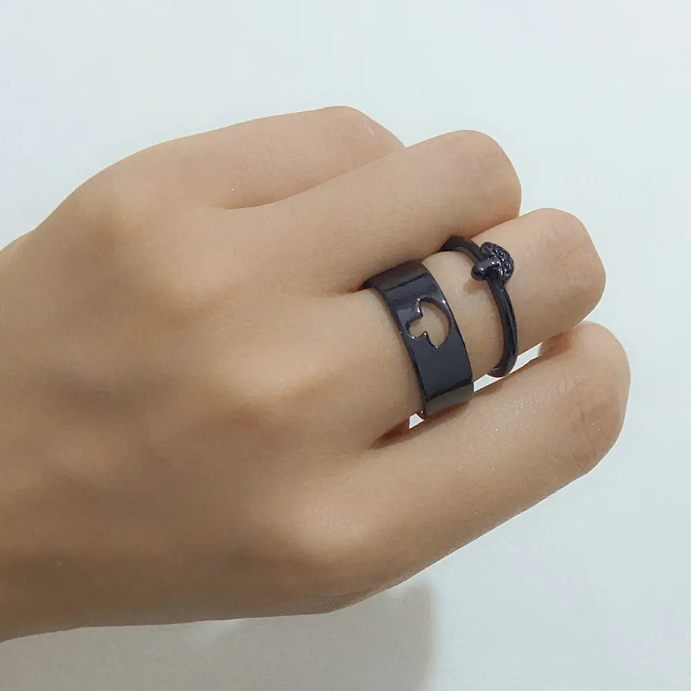Hand wearing a black ring with a unique design on a light gray background