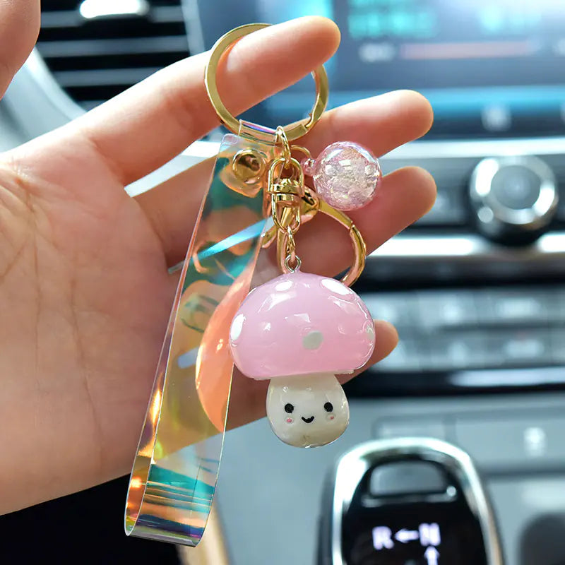 Hand holding a keychain with a pink mushroom charm in a car interior.