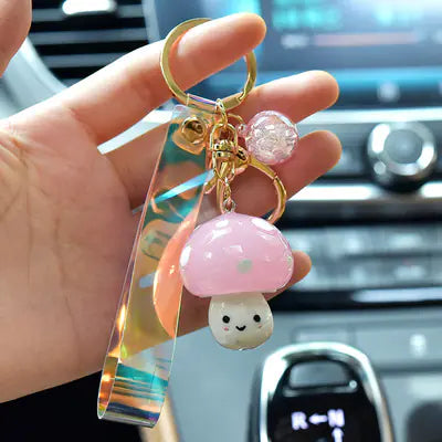 Keychain with a pink mushroom charm held by a hand in front of a car's dashboard.