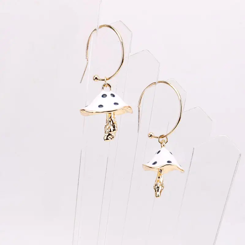 Mushroom-shaped earrings with gold and white design on a clear stand against a light gray background