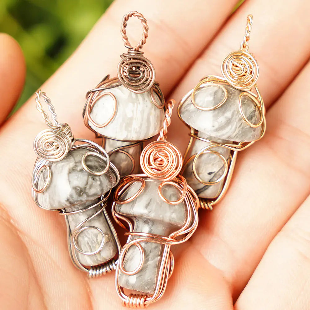 Four wire-wrapped stone pendants on a hand with a blurred green background
