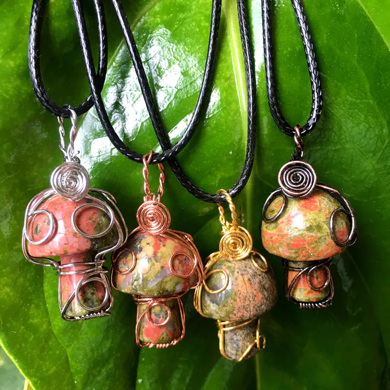 Four colorful stone pendants on black cords against a green leaf background