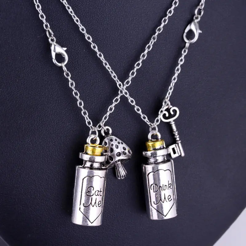 Two silver necklaces with 'Eat Me' and 'Drink Me' charms on a dark background