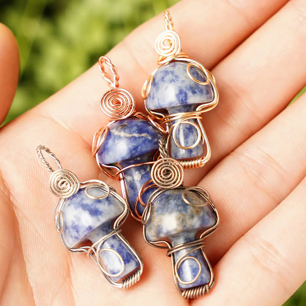 Blue stone pendants with gold wire wrapping held in a hand against a blurred green background