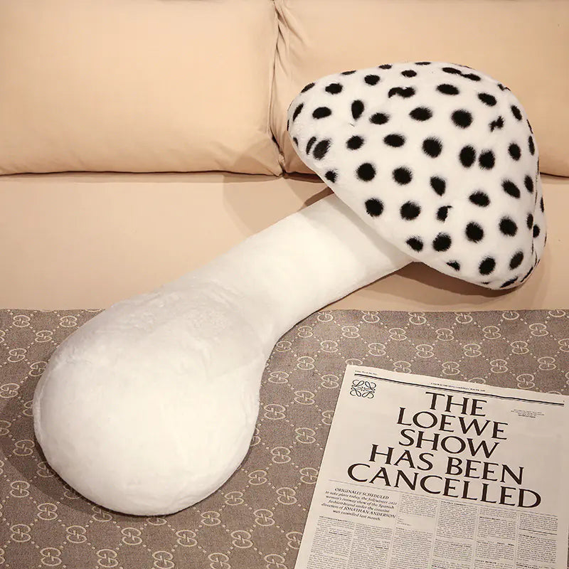 White and black polka dot mushroom-shaped pillow on a patterned surface with a newspaper.
