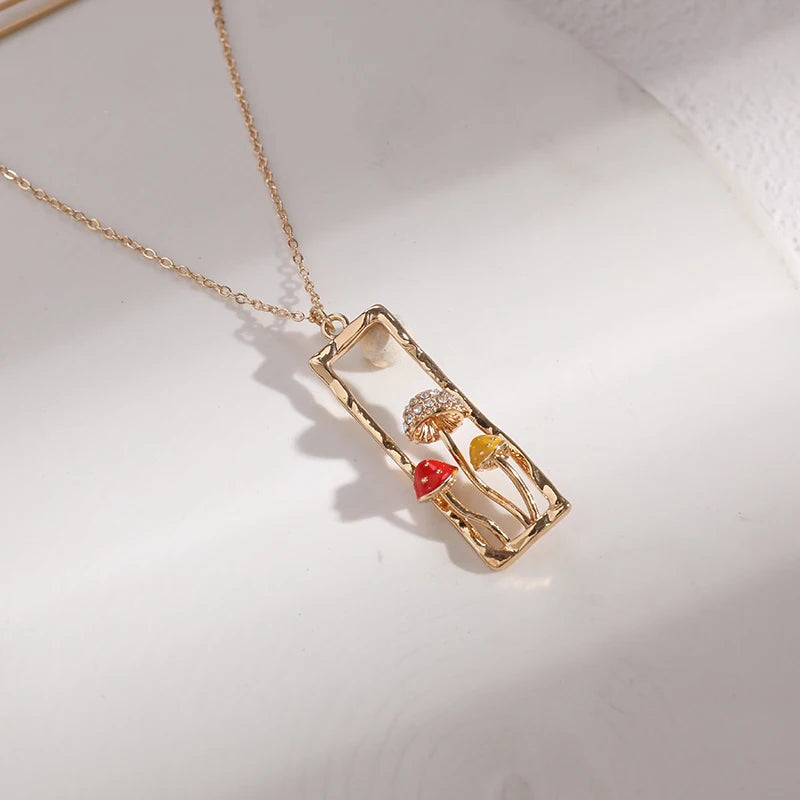 Gold necklace with a rectangular pendant featuring colorful mushroom designs on a light background