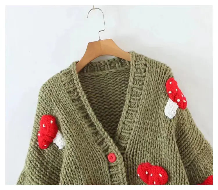 Knitted cardigan with mushroom designs on a hanger against a white background
