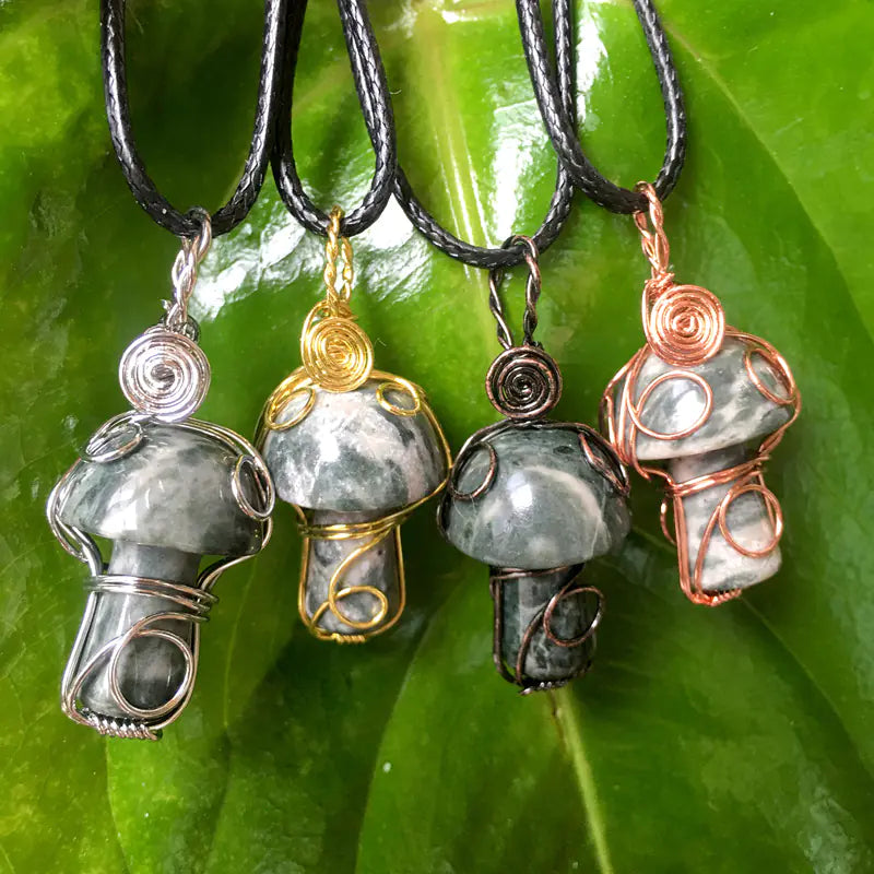 Four wire-wrapped stone pendants on black cords against a green leaf background