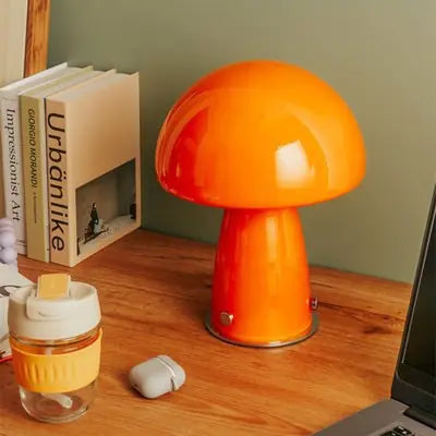 Orange mushroom-shaped lamp on a wooden desk with books and a glass container.
