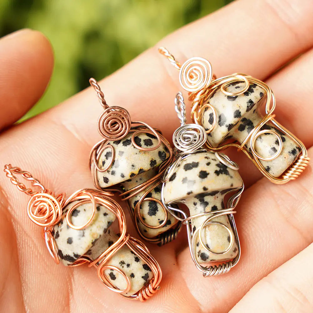 Hand holding three wire-wrapped dalmatian jasper mushroom pendants.