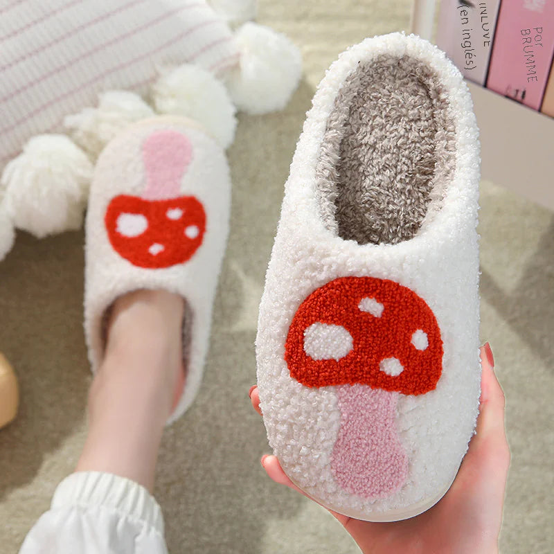 White slippers with red mushroom design held by a hand on a light background