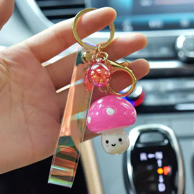 Keychain with pink mushroom charm held by a hand in front of a car interior.