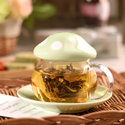 Glass teacup with a green lid filled with tea leaves on a woven mat.