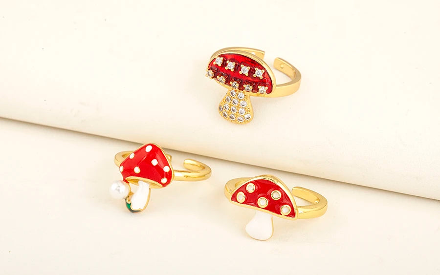 Three mushroom-shaped rings with red caps and gold bases on a white background