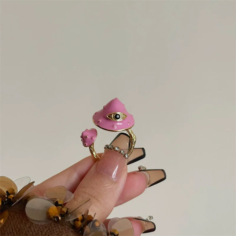 Hand holding a pink witch hat with an eye design and a small pink creature, against a plain background.
