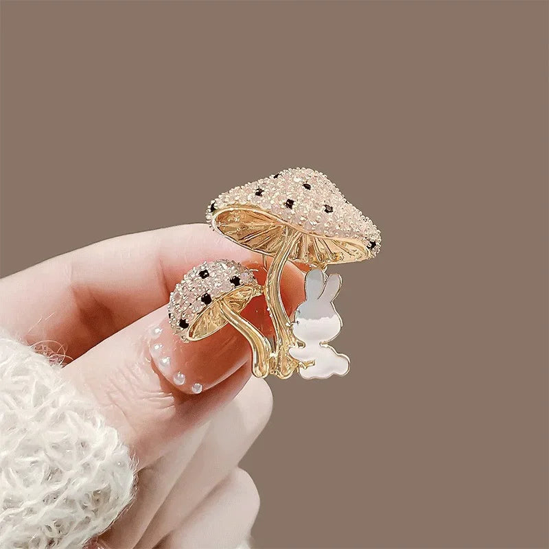 Gold mushroom-shaped brooch with a small rabbit figure held by a hand against a brown background