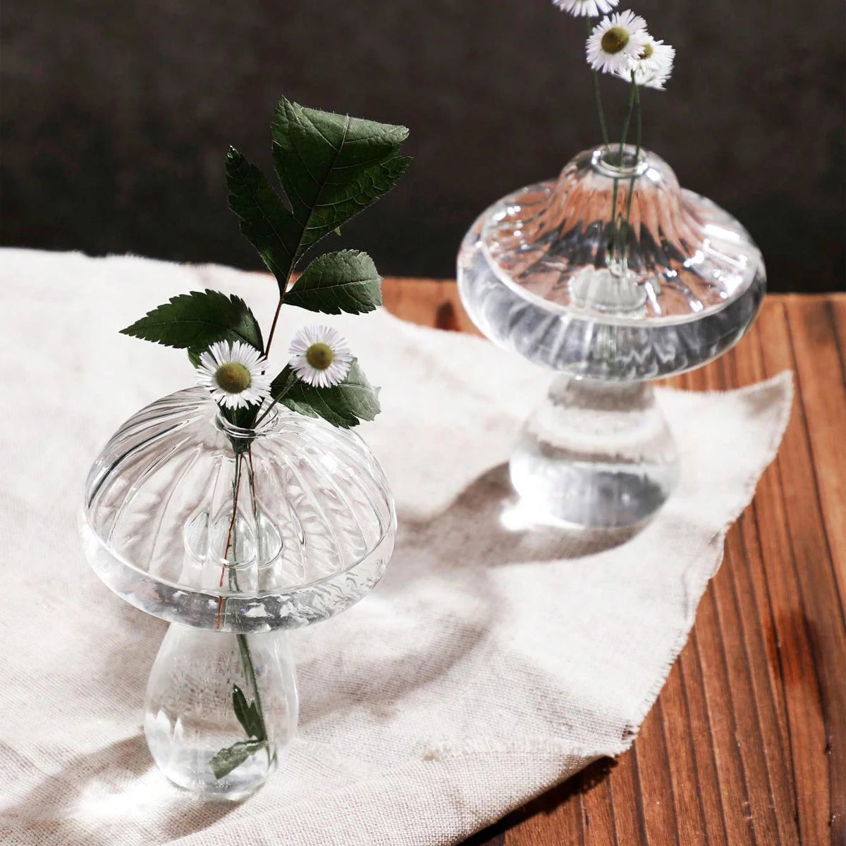 Two clear glass vases with flowers on a wooden surface