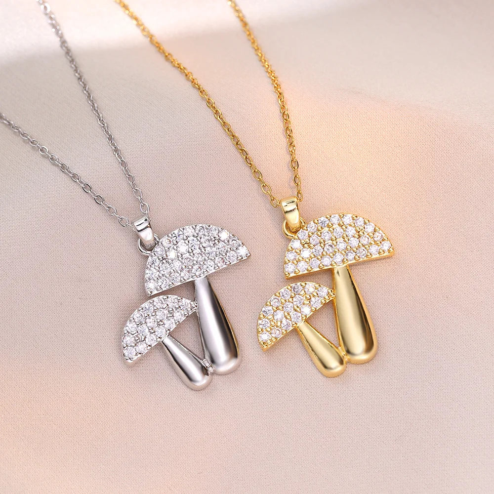 Two mushroom-shaped pendants, one silver and one gold, on a soft pink background.