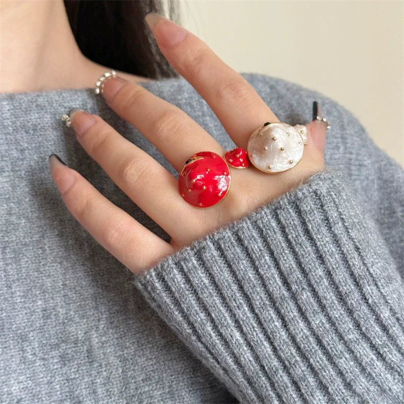 Close-up of a hand wearing two rings with red and white stones on a gray sweater.