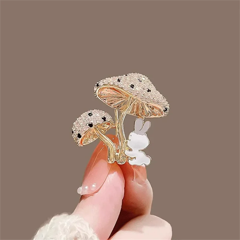 Decorative brooch with rabbit and mushroom design held by a hand against a brown background