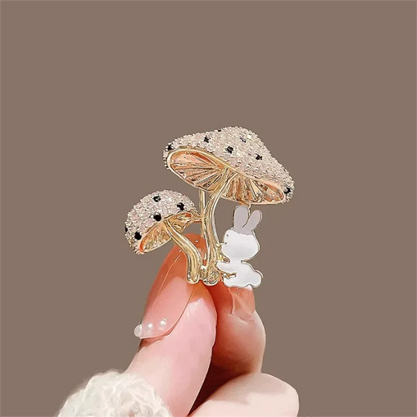 Decorative brooch with rabbit and mushroom design held by a hand against a brown background