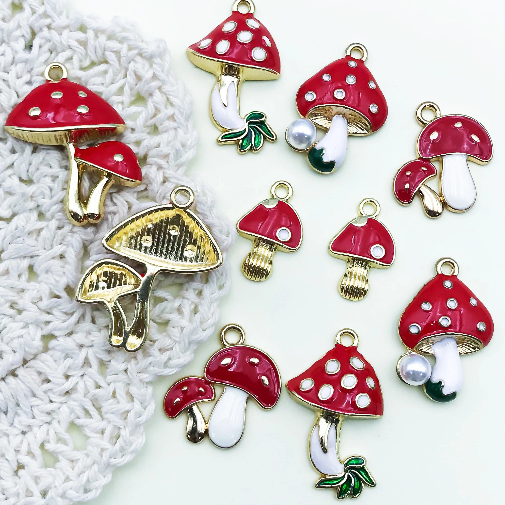 Mushroom-shaped charms with red caps, white stems, and gold bases on a textured white surface.