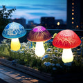 Three colorful mushroom-shaped lights on a garden bed with a cityscape in the background.