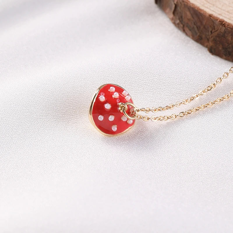 Red mushroom-shaped pendant with white polka dots on a gold chain against a white background.