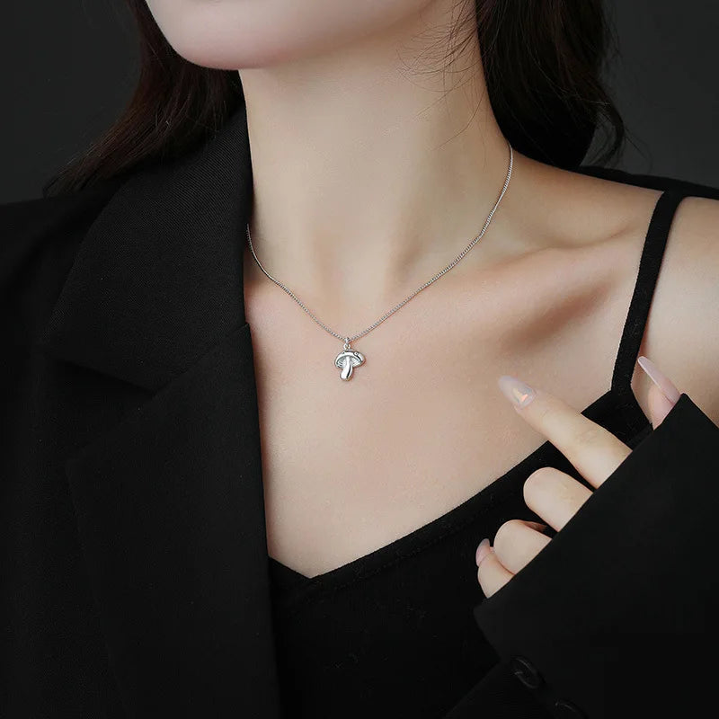 Person wearing a silver necklace with a leaf pendant against a dark background