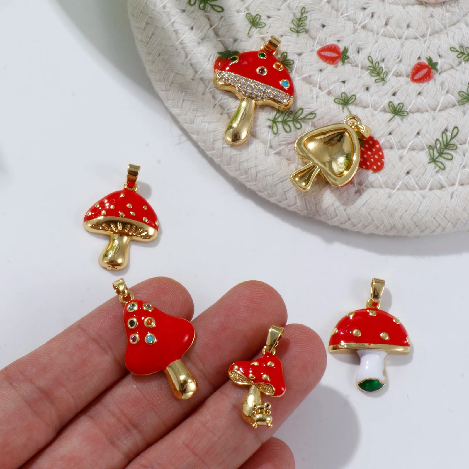 Red and gold mushroom-shaped pendants on a hand with a decorative plate in the background.