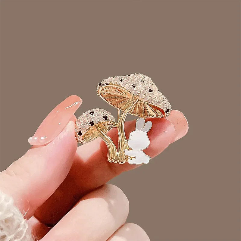 Gold mushroom-shaped brooch with a small rabbit figure held by a hand against a brown background