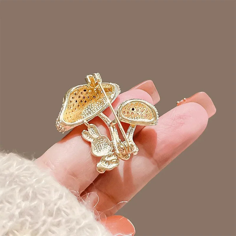 Gold mushroom-shaped brooch held by a hand against a brown background