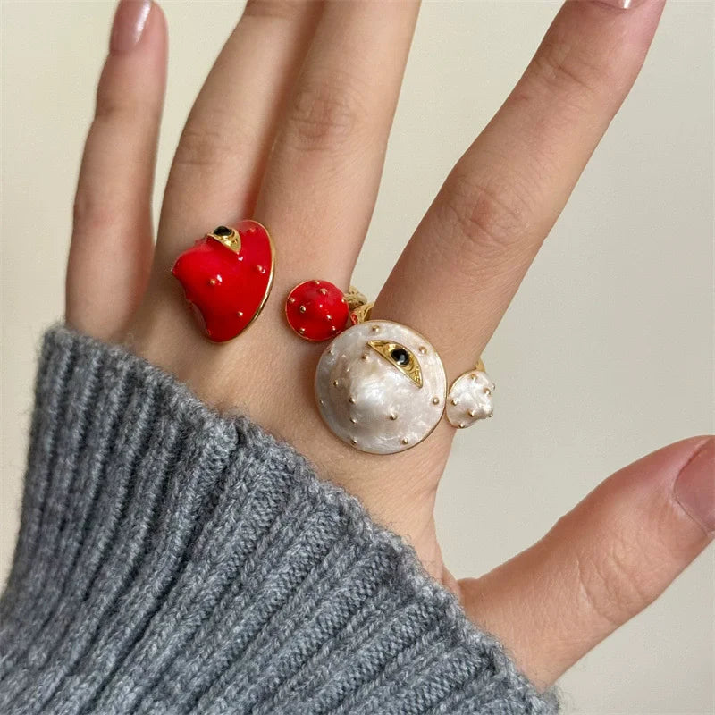 Hand wearing three rings with red and gold designs on a neutral background