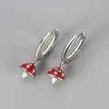 Silver earrings with red mushroom-shaped charms on a gray background