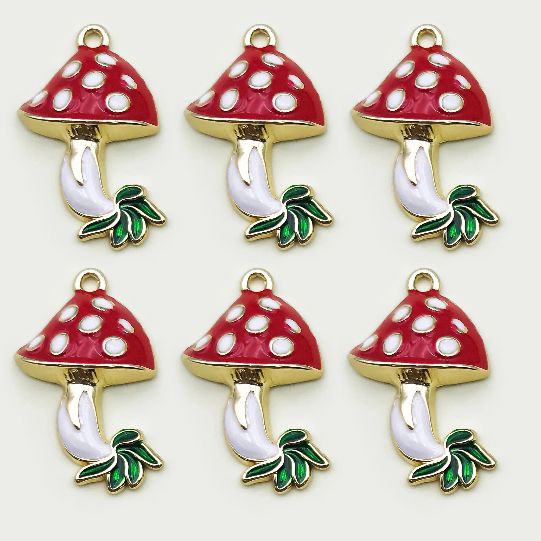 Six red mushroom-shaped charms with white spots on a gold base, green stems, and leaves on a white background.