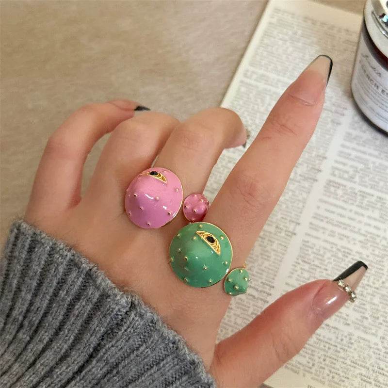 Hand wearing a ring with pink and green gemstones on a textured surface