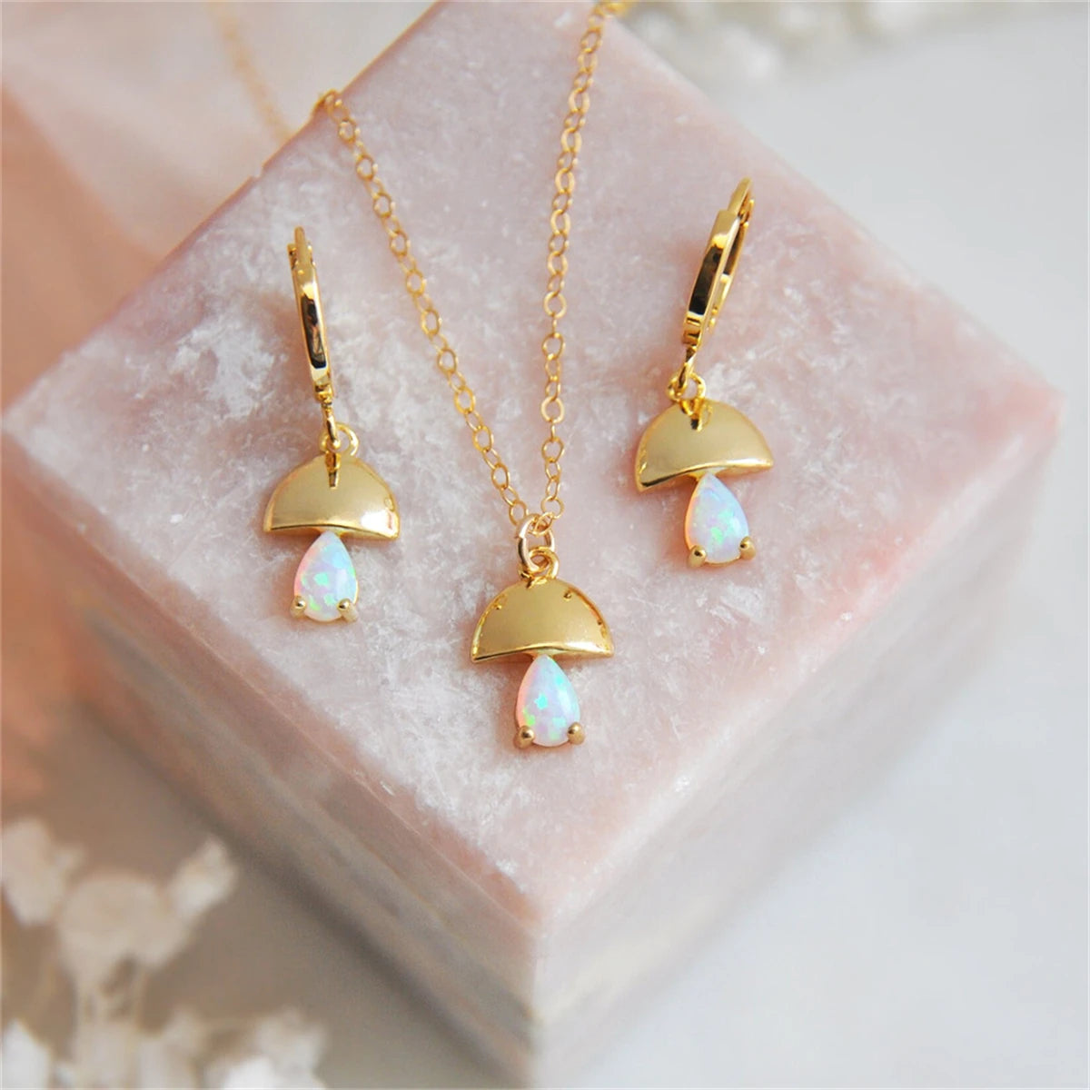 Gold jewelry set with opal stones on a pink stone surface