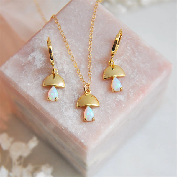 Gold jewelry set with opal stones on a pink stone surface