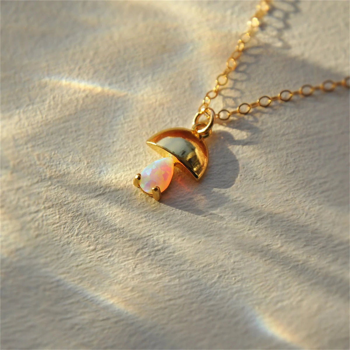 Gold necklace with a heart-shaped pendant on a textured beige surface