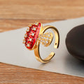 Gold ring with red gemstone and diamond accents on a wooden surface