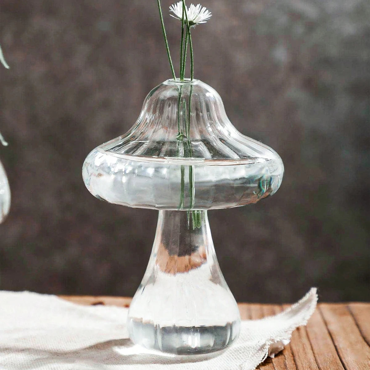 Clear glass vase shaped like a mushroom with flowers on a wooden surface