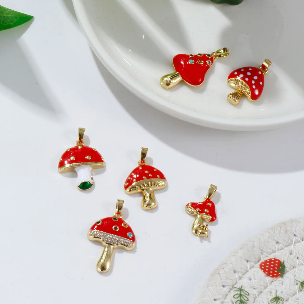 Red and gold mushroom-shaped pendants on a white surface with a green leaf.