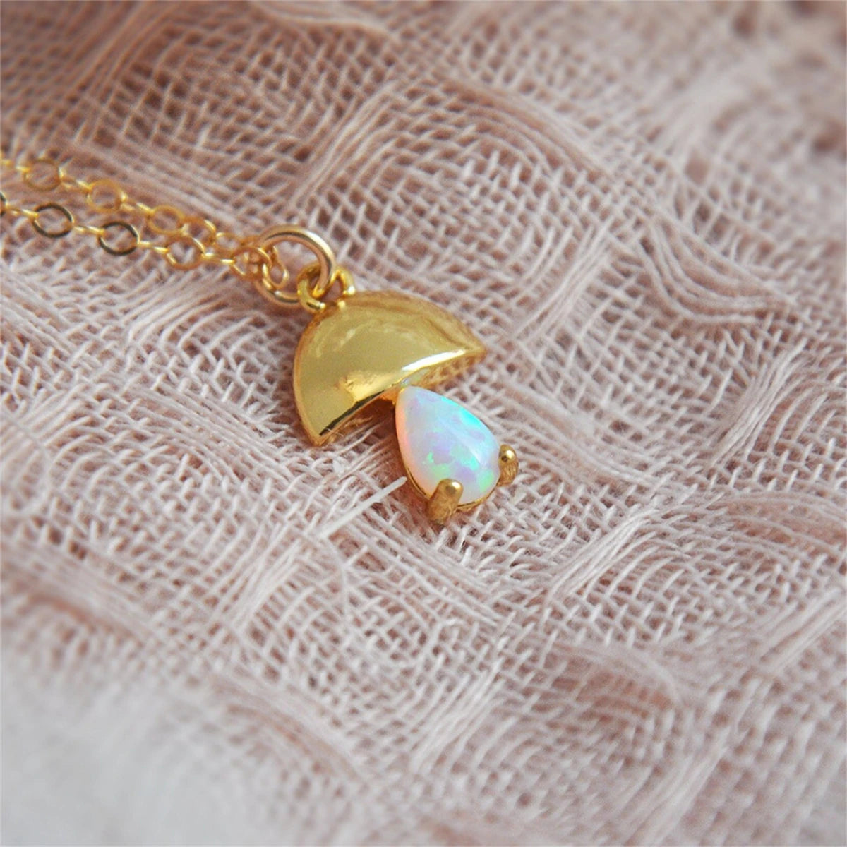 Gold necklace with a heart-shaped pendant featuring an opal stone on a textured fabric background