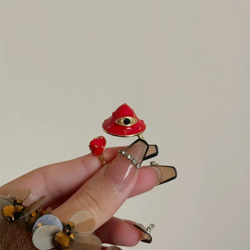 Hand holding a small red mushroom-shaped object with a black eye design against a plain background