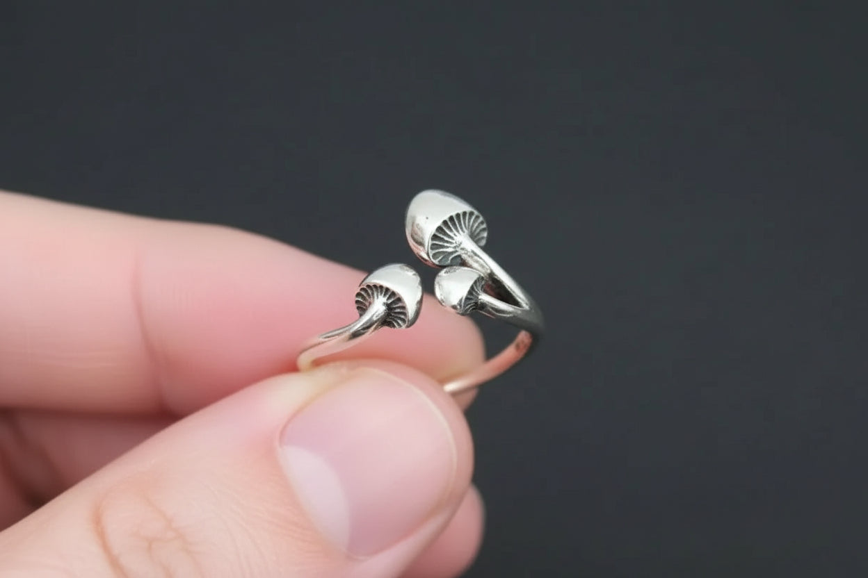 Silver mushroom-shaped ring on a hand against a dark background