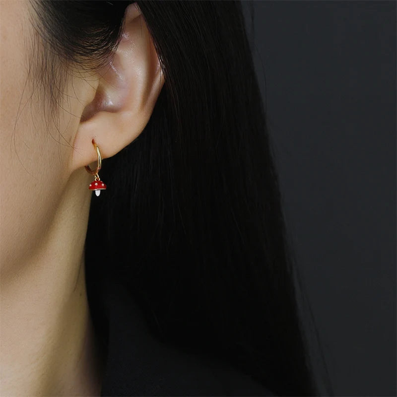 Close-up of an ear wearing a gold earring with a red gemstone on a dark background