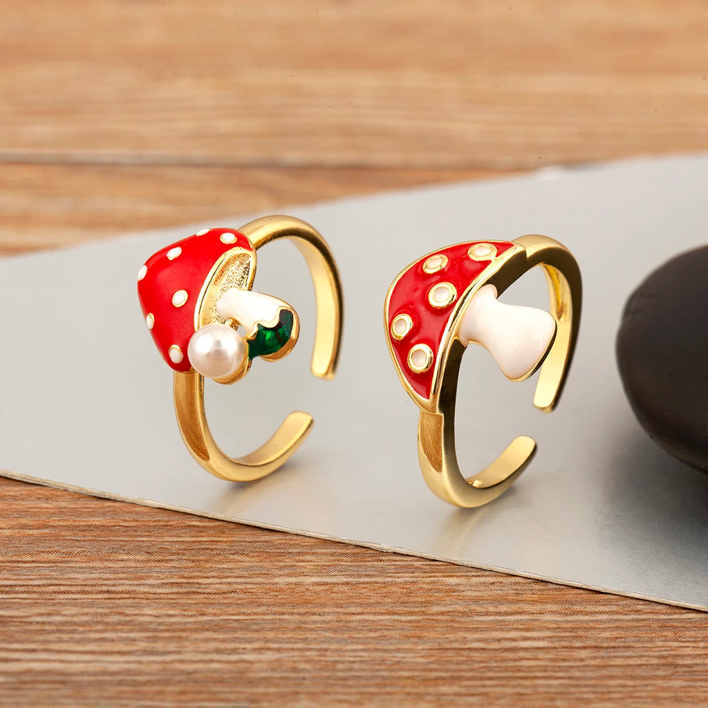 Pair of gold earrings with red mushroom-like tops and pearl centers on a wooden surface.