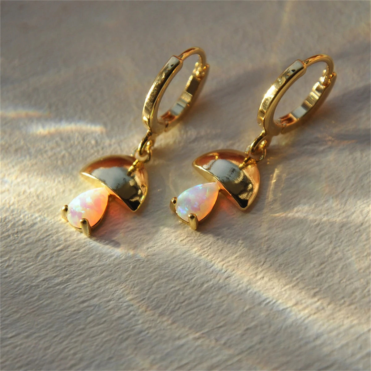 Gold earrings with opal stones on a textured beige surface